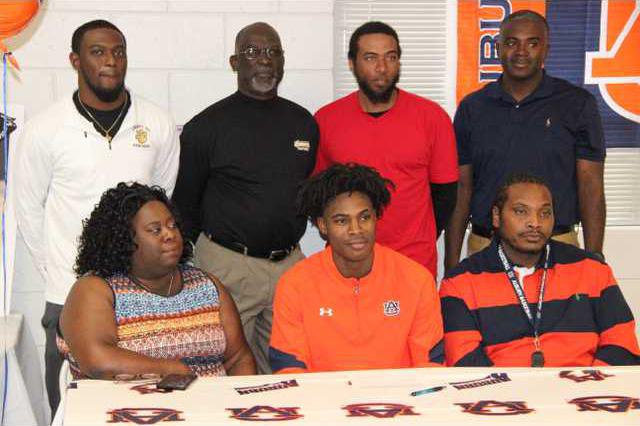 Davion Mitchell with his parents beside him and coaches behind him when he signed a letter to play basketball for Auburn